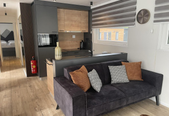 Moderne lodge ved Pressegger See, Østrig, med sort sofa, farverige puder og træ-inspireret køkken.