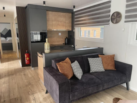 Lodge moderno Enzian en Pressegger See, Austria, con sofá negro, cojines y cocina de madera clara.