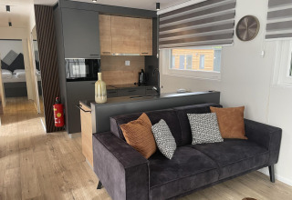 Lodge moderno Enzian en Pressegger See, Austria, con sofá negro, cojines y cocina de madera clara.