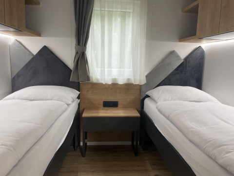 Twee eenpersoonsbedden met witte lakens in een moderne kamer bij lodge Enzian aan de Pressegger See, Oostenrijk.