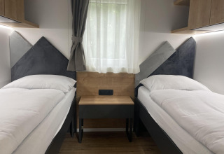 Twee eenpersoonsbedden met witte lakens in een moderne kamer bij lodge Enzian aan de Pressegger See, Oostenrijk.