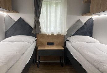Twee eenpersoonsbedden met witte lakens in een moderne kamer bij lodge Enzian aan de Pressegger See, Oostenrijk.