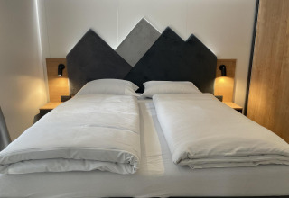 Cama moderna con cabecero en forma de montaña y edredones separados en Enzian, Pressegger See, Austria.