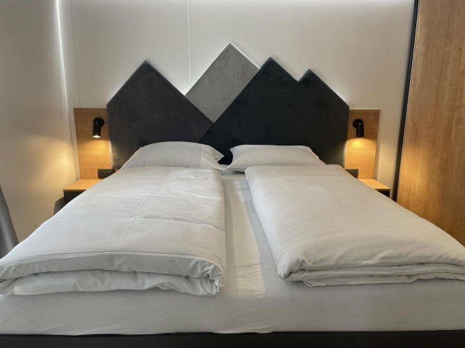 Cama moderna con cabecero en forma de montaña y edredones separados en Enzian, Pressegger See, Austria.