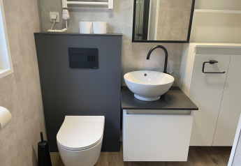 Modern badkamer met hangtoilet, ronde wastafel en spiegel in Enzian lodge aan Pressegger See, Oostenrijk.