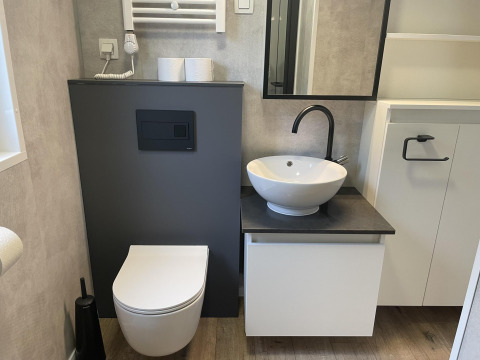 Salle de bain moderne avec toilettes murales, lavabo rond et miroir au lodge Enzian à Pressegger See, Autriche.