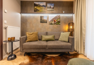 Acogedora sala en Enzian en Pressegger See, Austria, con sofá gris, cojines, arte mural y luz cálida.