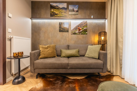 Salon confortable à Enzian au Pressegger See en Autriche, canapé gris, coussins, tableaux et lumière douce.