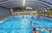 Piscina coperta con famiglie e bambini che giocano in acqua al Camping O2 in Normandia, Francia.