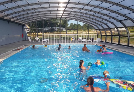 Piscina coperta con famiglie e bambini che giocano in acqua al Camping O2 in Normandia, Francia.