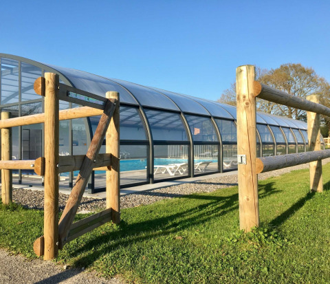 Enclosed swimming pool with wooden fence at Camping O2 holiday park in Normandy, France on a sunny day.