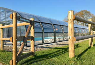 Enclosed swimming pool with wooden fence at Camping O2 holiday park in Normandy, France on a sunny day.