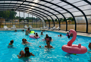 Überdachtes Schwimmbad mit spielenden Kindern und Flamingo-Boje im Camping O2, Normandie, Frankreich.