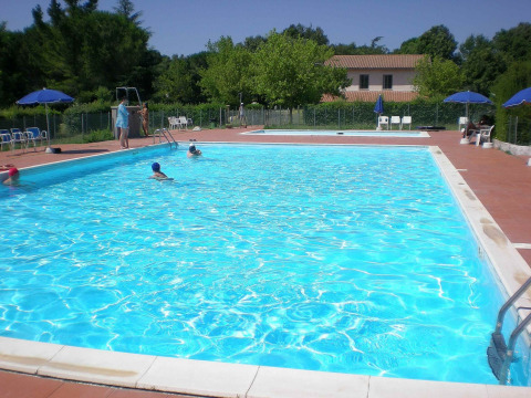 Außenpool im Camping Monti del Sole Ferienpark in Umbrien, Italien, mit Sonnenschirmen und Bäumen.