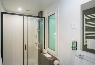 Baño moderno de Lodge con ducha, inodoro, ventana, toallero y espejo sobre el lavabo.