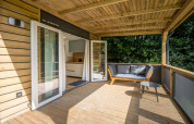 Træterrasse på Lodge at Urban-Gardens Ieper i Belgien med sofa, bord og udsigt til grøn natur.