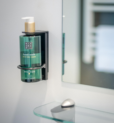 Dispenser di sapone verde Rituals montato a parete accanto a uno specchio in un bagno di lodge accogliente.