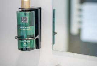Groene Rituals-handzeepdispenser aan de muur bij een spiegel, typisch gezien in een gezellige lodgebadkamer.