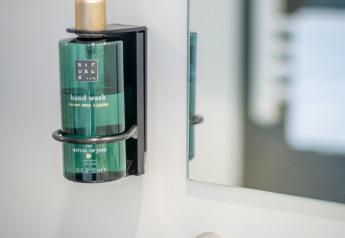 Groene Rituals-handwasdispenser aan de muur naast een spiegel in een gezellige lodge-badkamer gemonteerd.