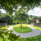Moderne houten lodges staan rond een grasveld met wandelpaden, omgeven door bomen en natuur.
