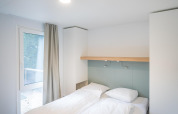 Et lyst og moderne soveværelse på en lodge, med en dobbeltseng, hvide sengetøj og naturligt lys.