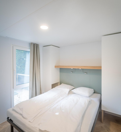 Et lyst og moderne soveværelse på en lodge, med en dobbeltseng, hvide sengetøj og naturligt lys.