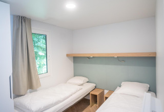 Camera di lodge luminosa e minimalista con due letti singoli, biancheria bianca, finestra e mobili in legno.