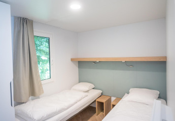 Habitación de alojamiento luminosa con dos camas individuales, ropa de cama blanca, ventana y muebles de madera.