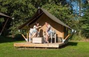 Dos personas disfrutan bebidas frente a una Glampingtent XS - IEPER en Urban-Gardens Ieper, Bélgica.