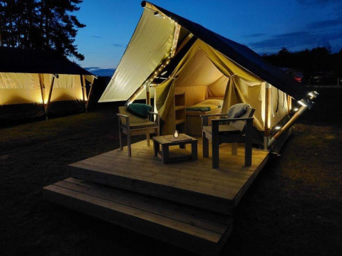 Tienda glamping safari iluminada con terraza y asientos en Urban-Gardens Ieper, Bélgica por la noche.