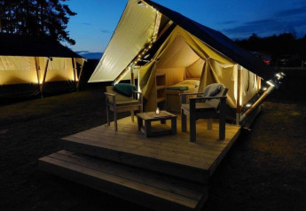 Tienda glamping safari iluminada con terraza y asientos en Urban-Gardens Ieper, Bélgica por la noche.