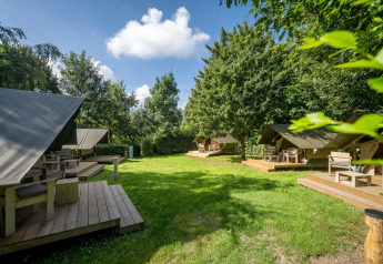 Glampingtent XS en Urban-Gardens Ieper, Bélgica, con terrazas de madera y mucho verde bajo el cielo azul.