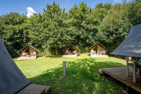 Tres pequeñas tiendas safari con terraza de madera rodeadas de verde en Urban-Gardens Ieper, Bélgica.