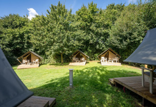 Drei kleine Glampingzelte mit Holzterrasse auf einer grünen Wiese bei Urban-Gardens Ieper, Belgien.