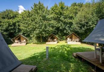 Drei kleine Glampingzelte mit Holzterrasse auf einer grünen Wiese bei Urban-Gardens Ieper, Belgien.