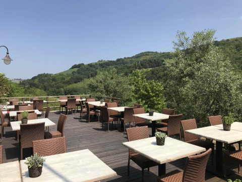 Terraza exterior de restaurante en Camping Podere sei Poorte en Marche, Italia, con mesas y vista a las colinas.