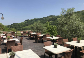 Terrasse extérieure de restaurant au Camping Podere sei Poorte dans les Marches, Italie, avec tables et vue vallonnée.