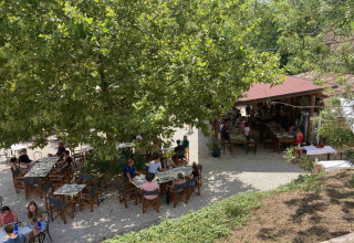 Udendørs spiseområde på Camping Podere sei Poorte i Marche, Italien, med gæster under store træer.