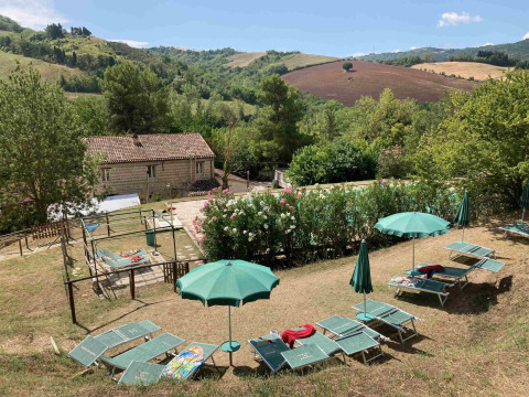 Lettini e ombrelloni verdi al Camping Podere sei Poorte tra le colline panoramiche delle Marche, Italia.