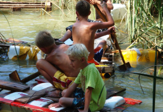 Kinderen spelen op een vlot van hout en piepschuim in het water bij Camping Podere sei Poorte, Marche, Italië.