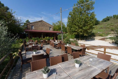 Zona pranzo all'aperto con tavoli e sedie in legno al Camping Podere sei Poorte, villaggio vacanze nelle Marche, Italia.