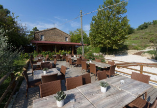 Udendørs spiseområde med træborde og stole på Camping Podere sei Poorte, feriested i Marche, Italien.