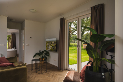 Modernes Wohnzimmer mit großen Fenstern, die auf einen grünen Garten im Vakantiepark Hölte blicken.