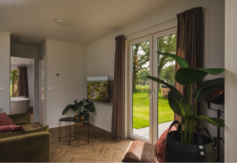 Knusse woonkamer van Panorama Lodge met grote ramen en tuinzicht in Vakantiepark Hölte, Nederland.