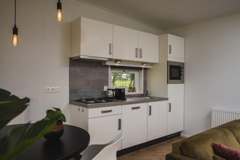 Moderne Küchenzeile mit weißen Schränken, kleinem Fenster und Essbereich in der Panorama Lodge Hölte.
