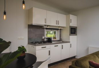 Moderne kitchenette met witte kasten, klein raam en zithoek in de Panorama lodge van Vakantiepark Hölte.