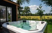Udendørs jacuzzi på Panorama Lodge med udsigt til marker, træer og himmel på Vakantiepark Hölte, Holland.