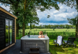 Donna che si rilassa in jacuzzi accanto a una tiny house a Panorama Lodge, Vakantiepark Hölte, Paesi Bassi, vista campi.