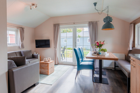 Lys og moderne lodge stue med sofa, spisebord og store vinduer i Vakantiepark Leukermeer, Holland.