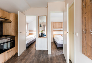 Moderna cabaña con puertas abiertas a los dormitorios, cocina y suelo de madera en Vakantiepark Leukermeer, Países Bajos.